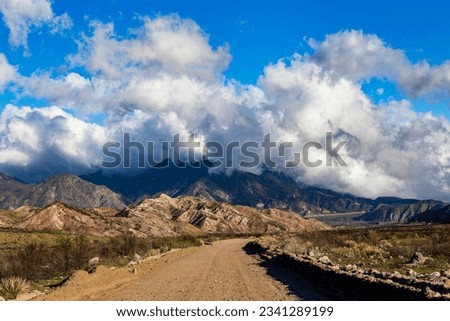 A mountain dirt road with clouds hugging the top and blue skies