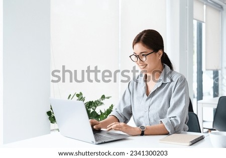 smiling pretty young asian business woman in spectacles sitting on workplace