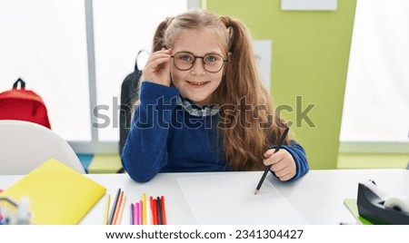 Adorable blonde girl student smiling confident drawing on paper at classroom