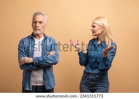 Unhappy marriage, crisis in relationships. Angry senior blonde woman wife scolding yelling at her frustrated offended husband grey-haired man, elderly couple fighting over beige studio background Royalty-Free Stock Photo #2341311773