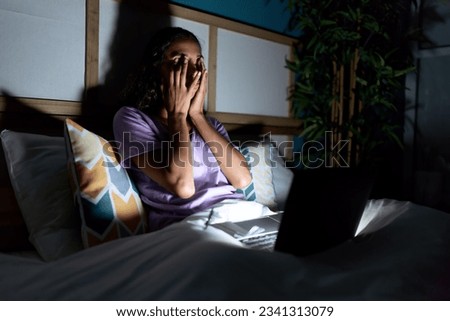 Young african american woman using laptop sitting on bed at bedroom