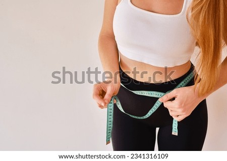 Young woman holds a measuring tape on her thin waist. Fitness instructor. The concept of nutrition, training and proper lifestyle. Beauty and weight loss Royalty-Free Stock Photo #2341316109