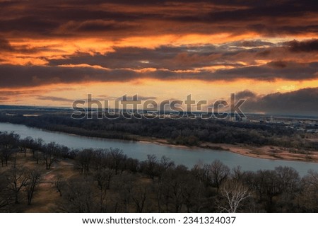 aerial shot of the flowing waters of the Mississippi River surrounded by bare winter trees and green trees with powerful clouds at sunset in Memphis Tennessee USA