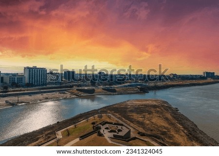 skyscrapers and office buildings in the city skyline along the banks of Wolf Creek Harbor with silky green waters and red sky with powerful clouds at Mud Island Park in Memphis Tennessee USA