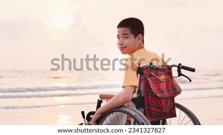 Asian boy with happy face on the sunset sea beach, Beautiful moment nature,Traveling using a wheelchair to learn about the world without limits with support from family,Good mental health,positive pic