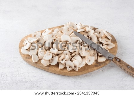 Wooden board with sliced champignon mushrooms on a light gray background, cooking vegan food. Royalty-Free Stock Photo #2341339043