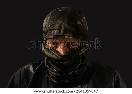 Military man with a dirty face and a camouflage mask. The concept of a man after military action or fraud, robbery. Closeup. Human on a dark background. Royalty-Free Stock Photo #2341359847