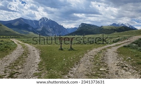 Fork in the Road: Dirt Road Splits At Sign Junction, High Alpine Mountain Landscape Royalty-Free Stock Photo #2341373631