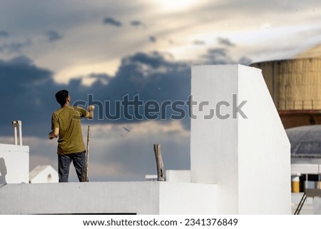 Jaipur, Rajasthan - 14th Jan 2023: Slow motion shot of man on roof of white building flying kite with multiple kites visible in background during the festival of sankranti, uttarayan and independence  Royalty-Free Stock Photo #2341376849