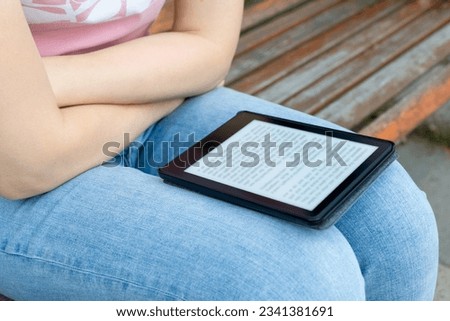  woman reading an e-book sitting on a park bench. reading a book built on electronic ink technology. High quality photo