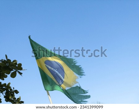 Flag of Brazil worn by the wind waving in blue sky.