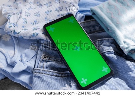 Different clothes and a smartphone with green screen, top view. Concept of traveling or shopping online