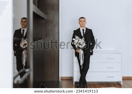 portrait. A man in a white shirt, black suit poses in a white room, holding a bouquet. A stylish watch. Men's style. Fashion. Business