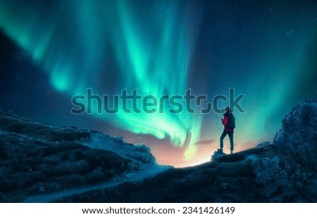 Northern lights and woman on mountain peak at night. Aurora borealis and silhouette of alone girl on mountain trail. Landscape with polar lights. Sky with stars and bright aurora. Travel background