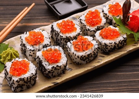 Sushi roll with red caviar on a plate with wasabi, ginger, maple leaves and chopsticks for sushi, on a wooden background