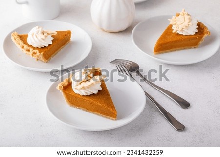 Slice of a traditional pumpkin pie for Thanksgiving topped with whipped cream on light background