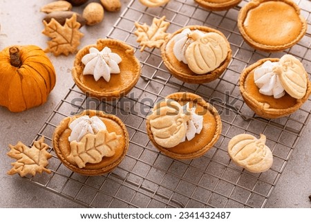 Mini pumpkin pies for Thanksgiving topped with leaves and pumpkin garnishes and whipped cream