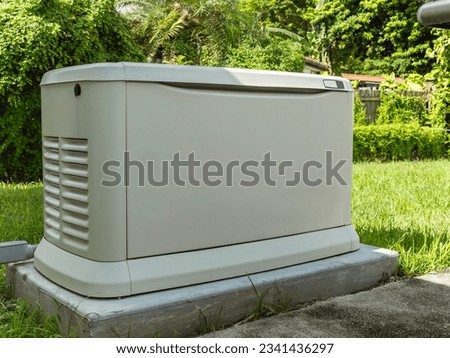 A Home Standby Generator installed at the backyard of a house. An air-cooled natural gas or liquid propane generator for residential use. Royalty-Free Stock Photo #2341436297