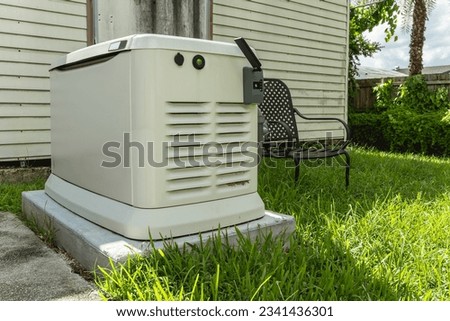 A Home Standby Generator installed at the backyard of a house. An air-cooled natural gas or liquid propane generator for residential use. Royalty-Free Stock Photo #2341436301
