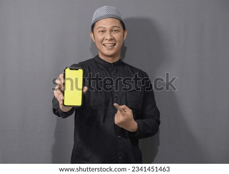 Happy muslim asian man wearing black muslim shirt showing green screen mobile phone