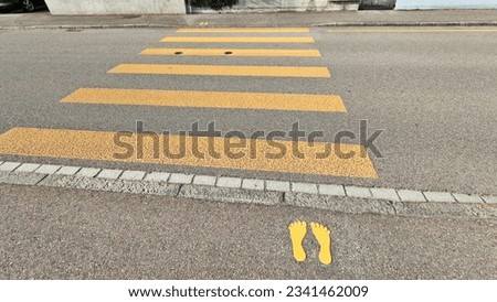 Yellow pedestrian crossing with yellow footprint road markings feet.