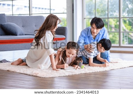 Asian happy cheerful joyful family husband and wife lover couple sitting on carpet floor helping teaching little boy son and girl daughter painting drawing cartoon with color pencils in living room.