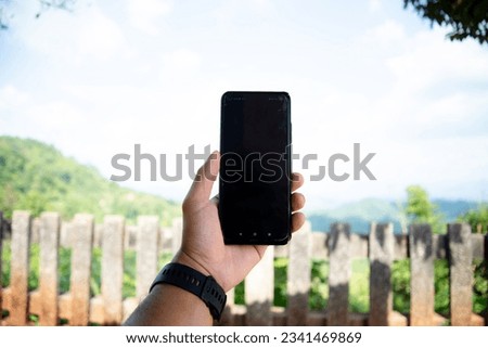 Man holding smartphone showing Black blank screen with the landscape mountain and sky cloudy day. travel communication and technology concept. 
