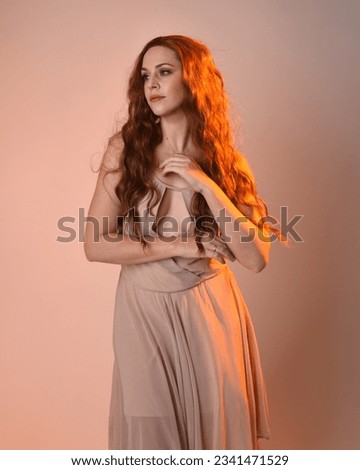 Close up portrait of beautiful brunette  female model wearing a cream dress with golden back light lighting.
Gestural arm poses with hands reaching out, isolated on studio background.

