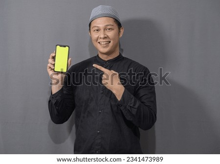 Happy muslim asian man wearing black muslim shirt showing green screen mobile phone