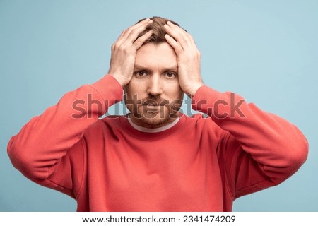 Puzzled confused bearded man holds head looking at camera on blue background. Guy having problems, life troubles. Midlife crisis, misfortune, sadness, grief, sorrow, negative human emotions concept. Royalty-Free Stock Photo #2341474209