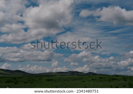 Photo of the steppe in summer, with beautiful clouds in the blue sky, the endless steppe at the foot of high hills under a warm summer sky. Khakassia, Siberia, Russia.