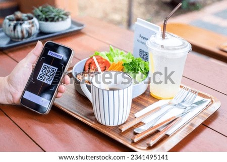 Customer hand using smart phone to scan Qr code payment tag with blur coffee and salad on wooden table to accepted generate digital pay without money. Qr code payment concept.