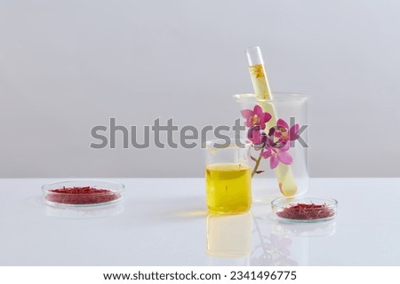 Glass petri dishes of saffron displayed with a beaker and test tube filled with liquid. Few Crocus flowers featured. Empty area for cosmetic product presentation