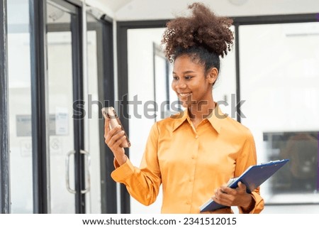 Portrait of an Asian smiling businesswoman standing holding and using a smartphone.