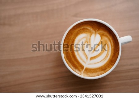 Top view of hot latte coffee with latte art in the white cup on the wooden table. Copy space. Royalty-Free Stock Photo #2341527001