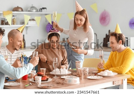 Young woman cutting Birthday cake at party with her friends