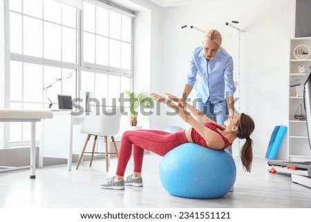 Young woman training with female physiotherapist on fitball in rehabilitation center Royalty-Free Stock Photo #2341551121