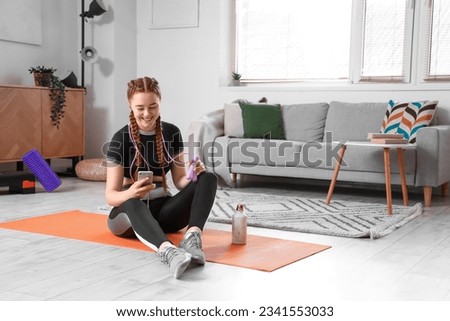 Sporty young woman with skipping rope using mobile phone at home Royalty-Free Stock Photo #2341553033