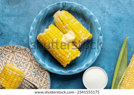 Plates of boiled corn cobs with butter on blue background Royalty-Free Stock Photo #2341555175