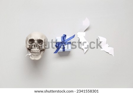 Composition with beautiful gift box, skull and bats made of paper for Halloween on light background