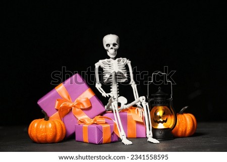 Beautiful gift boxes, skeleton, pumpkins and lantern for Halloween on dark background, closeup