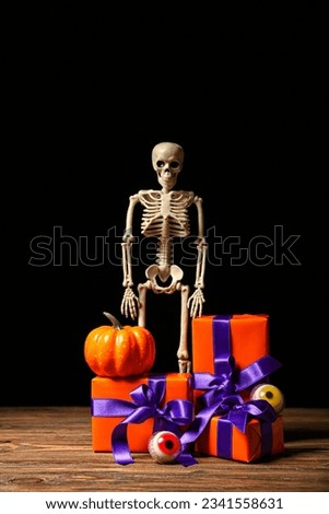 Beautiful gift boxes, skeleton, pumpkin and tasty candies for Halloween on wooden table against dark background