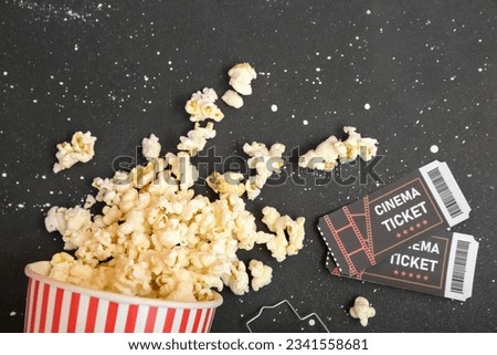 Bucket with tasty popcorn and cinema tickets on dark background, closeup. Halloween celebration