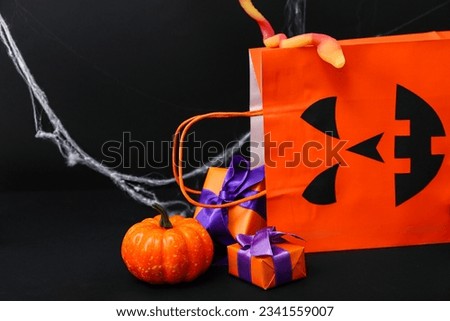 Composition with shopping bag, gift boxes and pumpkin for Halloween on dark background