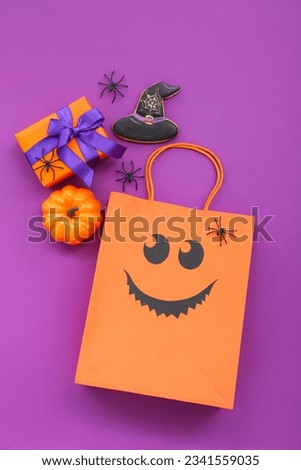 Composition with shopping bag, gift box, pumpkin and tasty cookie for Halloween on purple background
