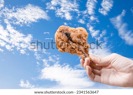 Crispy fried chicken in hand on sky background.  Royalty-Free Stock Photo #2341563647