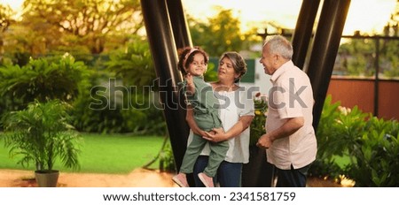 Happy Indian old grandmother standing holding cute little child girl in arms hands playing together outdoor home. Beautiful senior couple talking with small adorable daughter enjoying summer holiday Royalty-Free Stock Photo #2341581759