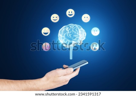 Emotional intelligence concept. Polygonal human brain and various human emotions: fear, surprise, joy, sadness, anger. Close up of male hand holding cellphone with hologram on blurry background