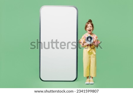 Full body fun little child kid girl 6-7 years old wear casual clothes big blank screen area mobile cell phone scream in megaphone isolated on plain green background. Mother's Day love family concept