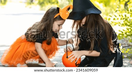 Two little cute girl in witch costume holding jack-o-lantern pumpkin bucket. Kids trick or treating in Halloween holiday.